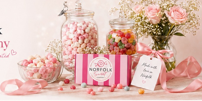 Pastel sweet display with glass jars, pink sweets, flowers and Norfolk Sweet Company gift packaging